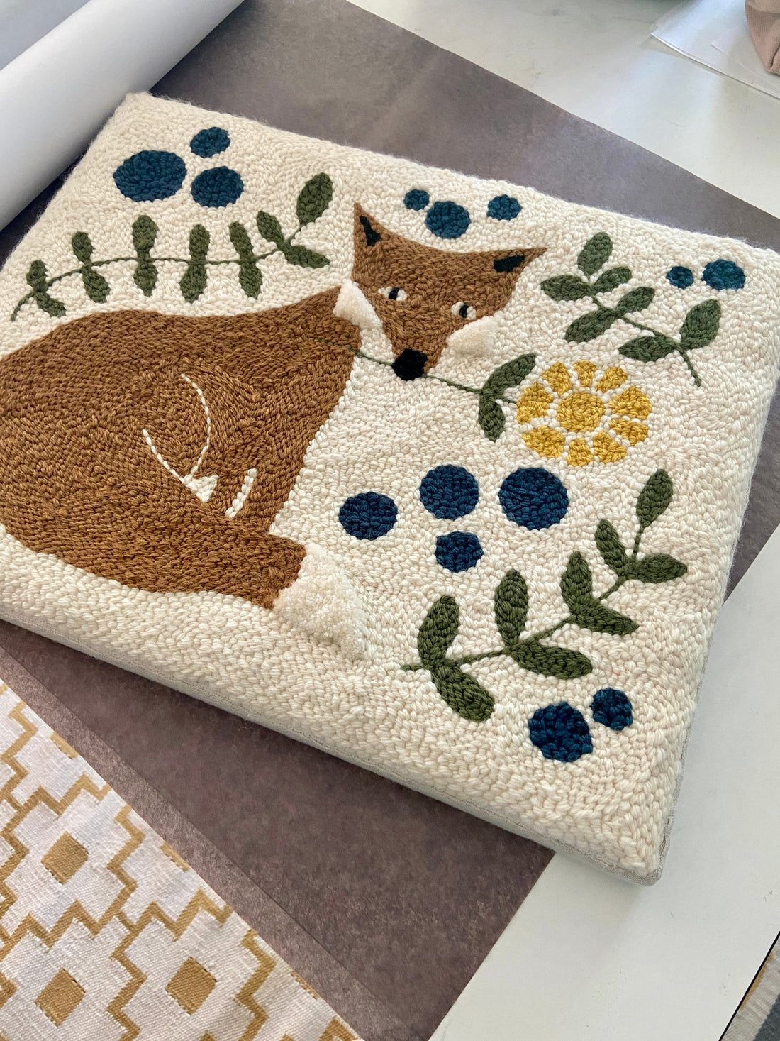 Folk style textile artwork featuring a fox with a flower in his mouth surrounded by plants