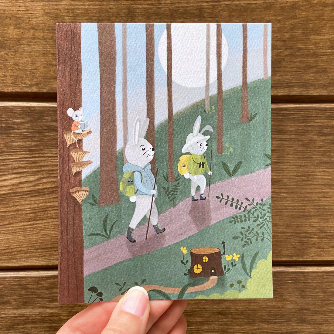 Magical greeting card featuring two rabbits hiking in the woods