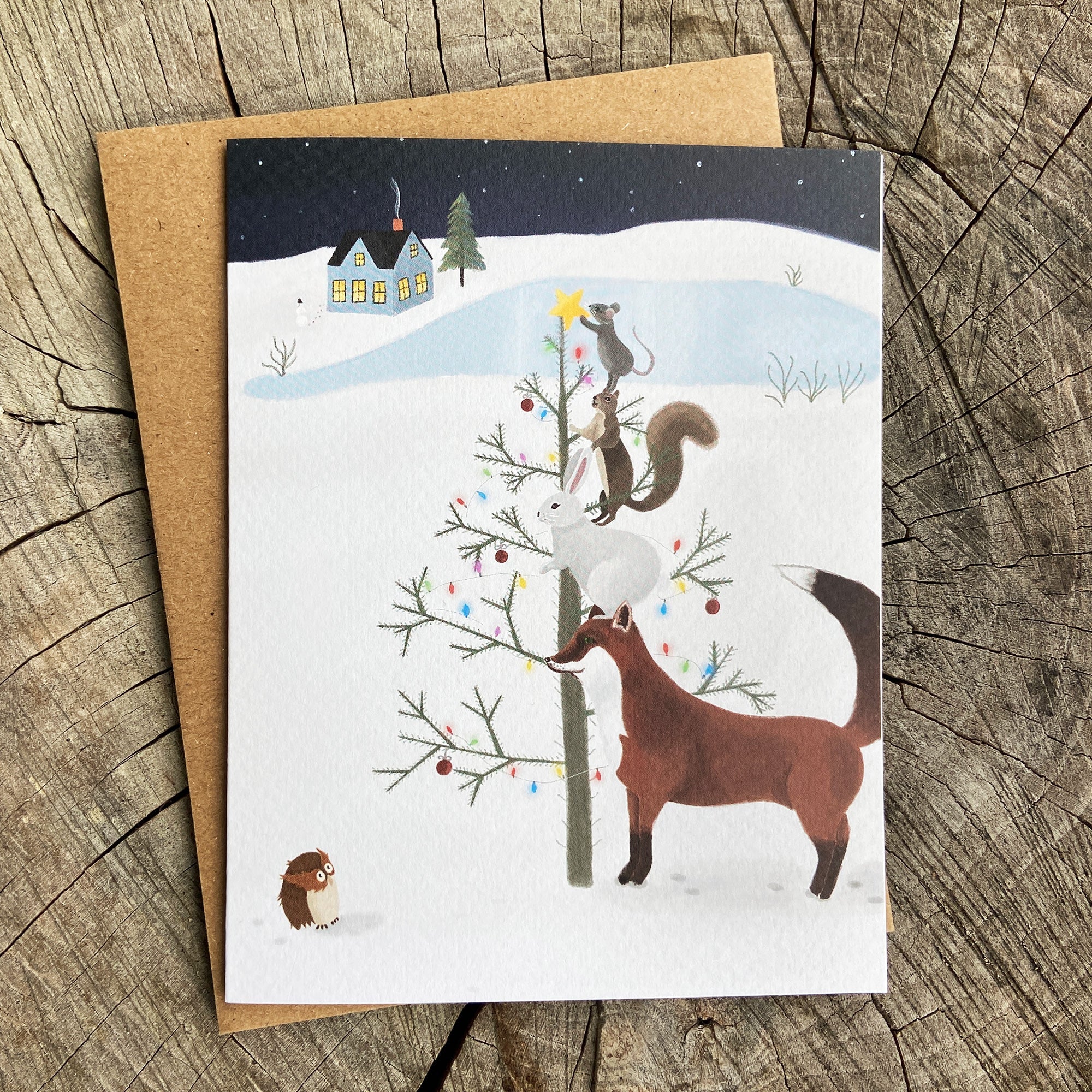 Holiday card with winter scene featuring woodland animals decorating a tree.