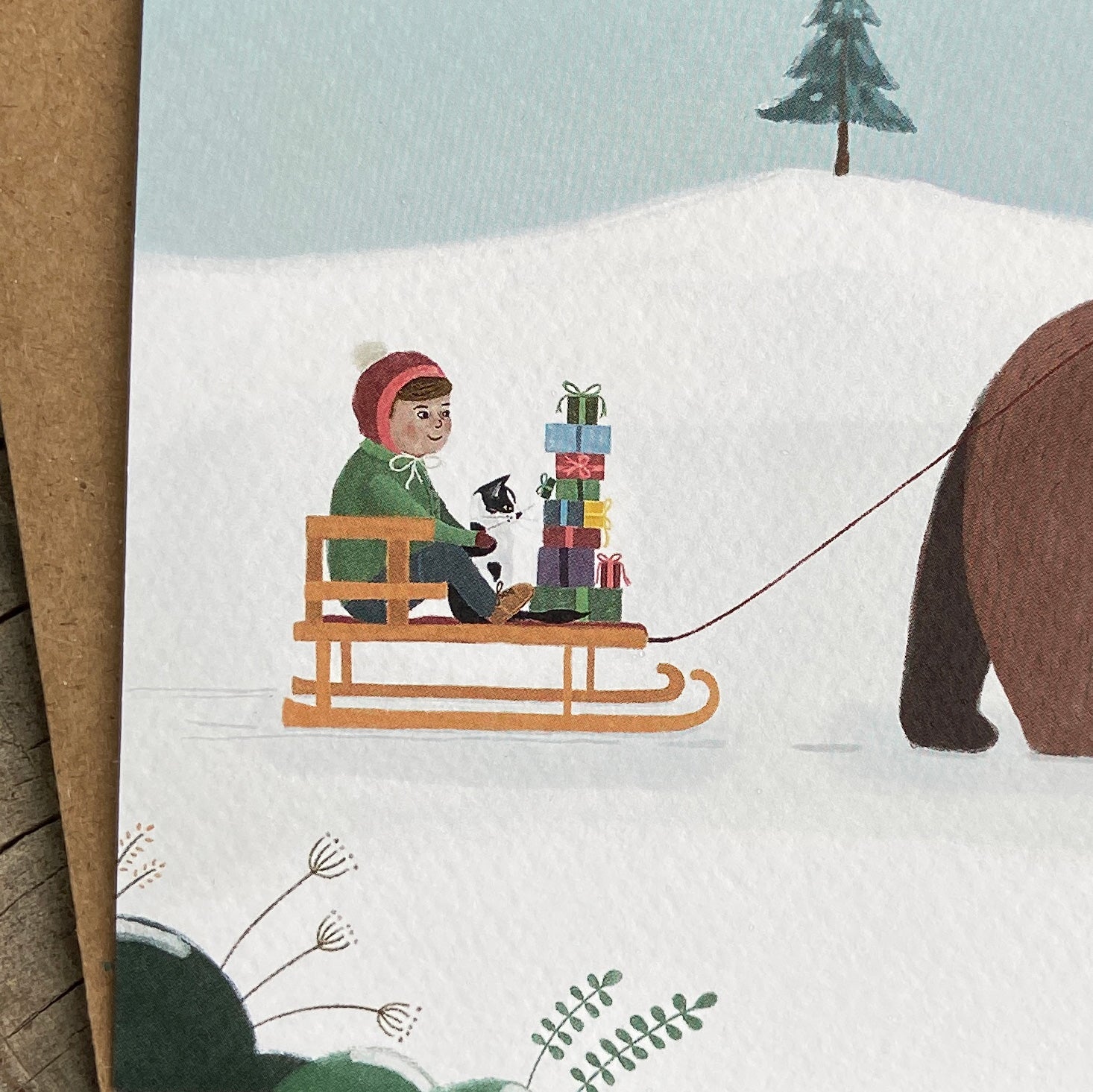 Illustration of a child on a sled with gifts, pulled by a bear, in a snowy landscape.