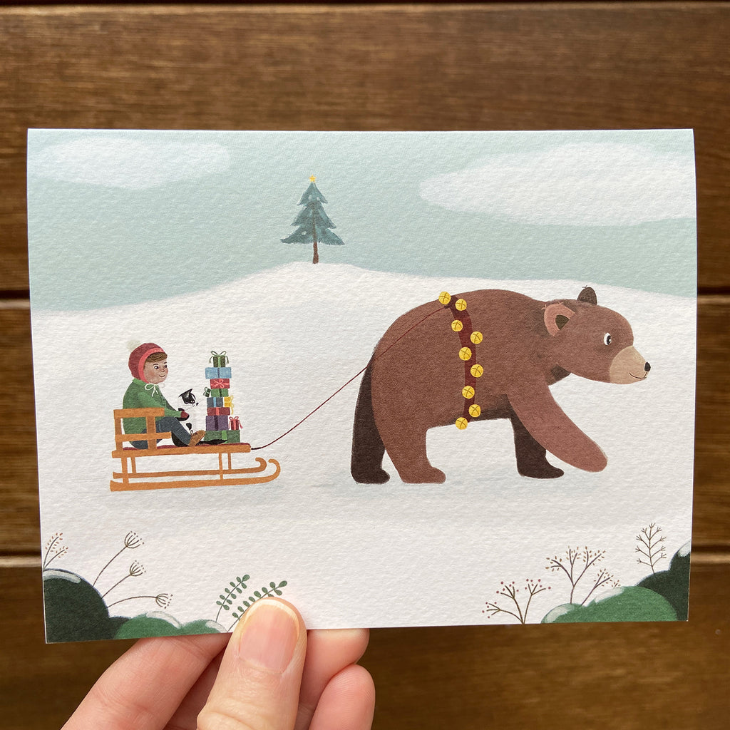 Illustrated card with a bear pulling a sled with a child, cat and stack of gifts