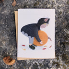Fall greeting card with a child in a bat costume picking up a pumpkin, placed on a textured stone surface.