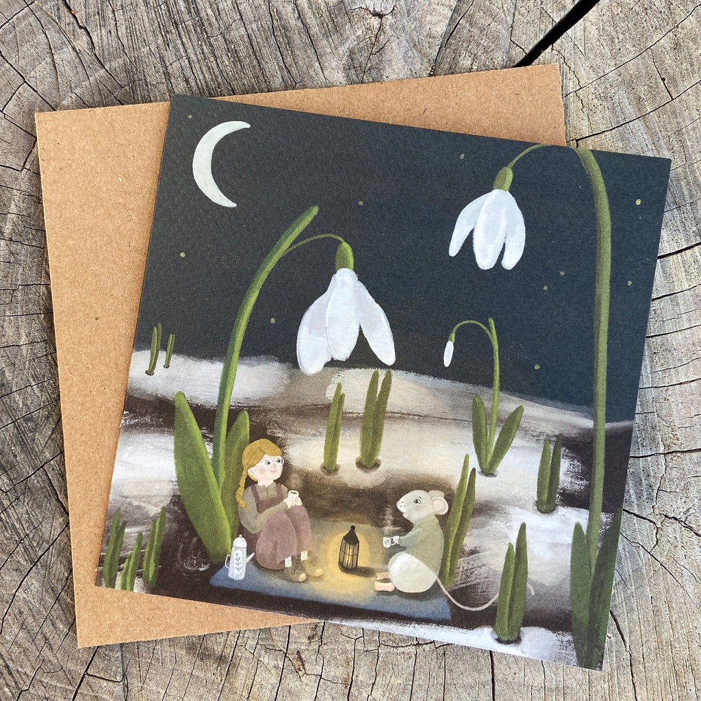 Greeting card with illustration of a girl and mouse drinking tea in a snowdrop garden, on a wooden surface
