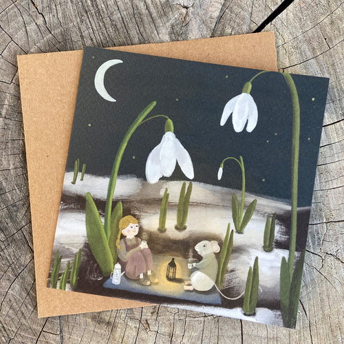 Greeting card with illustration of a girl and mouse drinking tea in a snowdrop garden, on a wooden surface