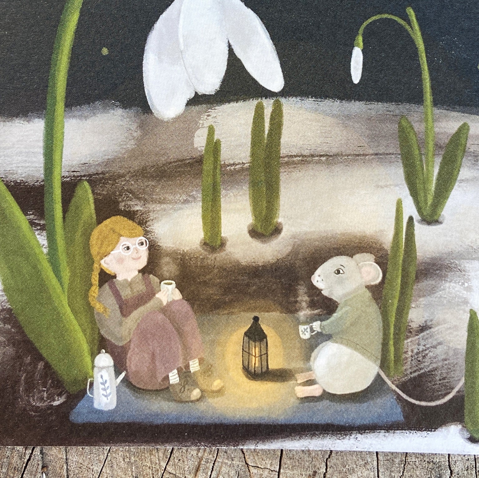 Close up of an illustrated greeting card featuring a girl and a mouse by a lantern at night with snowdrops in the background