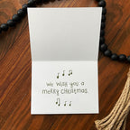 Christmas card with 'We wish you a merry Christmas' text on a wooden surface.