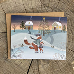 Greeting card with a mom fox helping her baby fox ice skate in a magical winter scene.