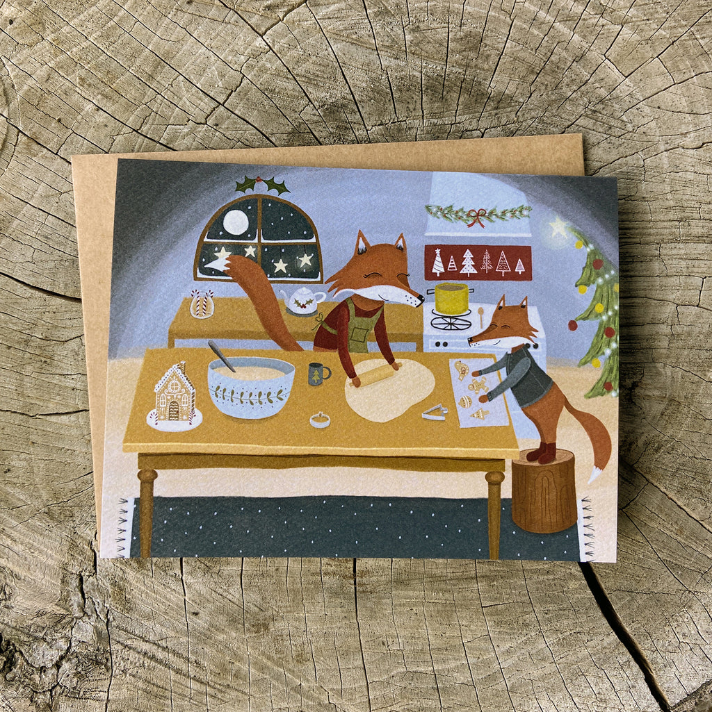 Holiday greeting card with illustration of two foxes baking cookies, on a wooden surface