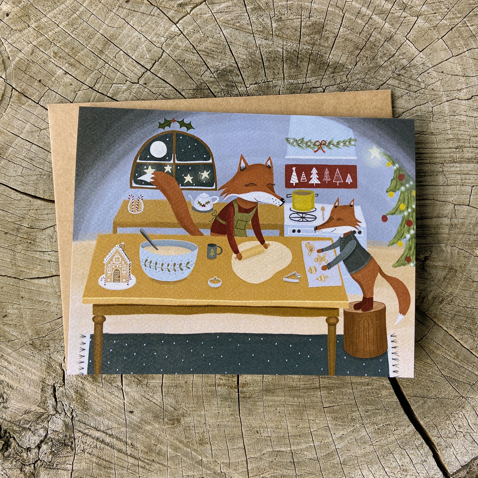 Holiday greeting card with illustration of two foxes baking cookies, on a wooden surface