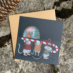 Greeting card with Christmas illustration of mice holding a candy cane, on a textured stone surface.