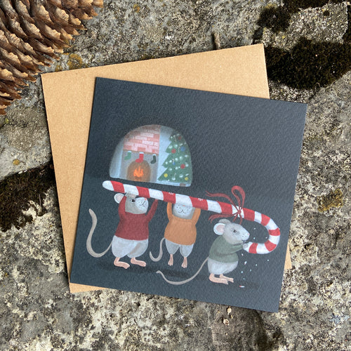Greeting card with Christmas illustration of mice holding a candy cane, on a textured stone surface.