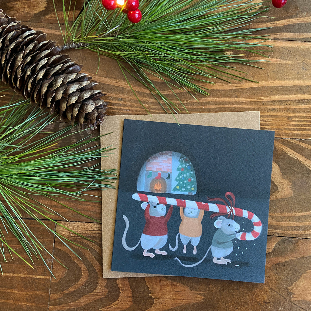 Greeting card with Christmas-themed illustration of mice and candy canes on a wooden surface with pine branches and pinecones.
