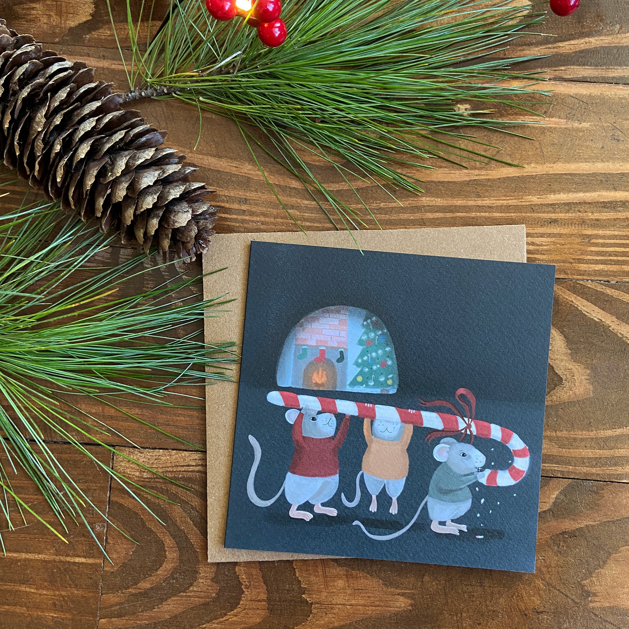 Greeting card with Christmas-themed illustration of mice and candy canes on a wooden surface with pine branches and pinecones.