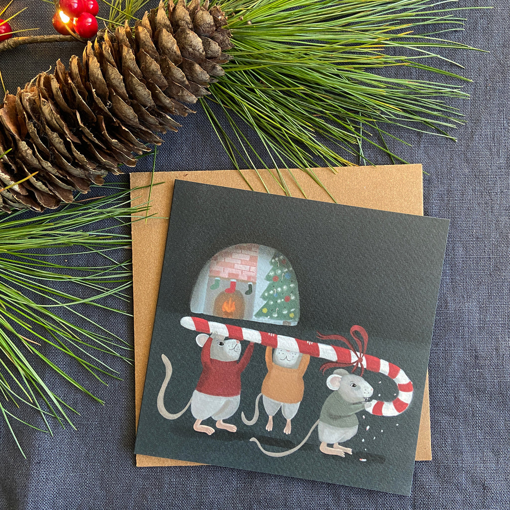 Christmas card with mice holding a candy cane, surrounded by pine cones and branches on a gray fabric background.