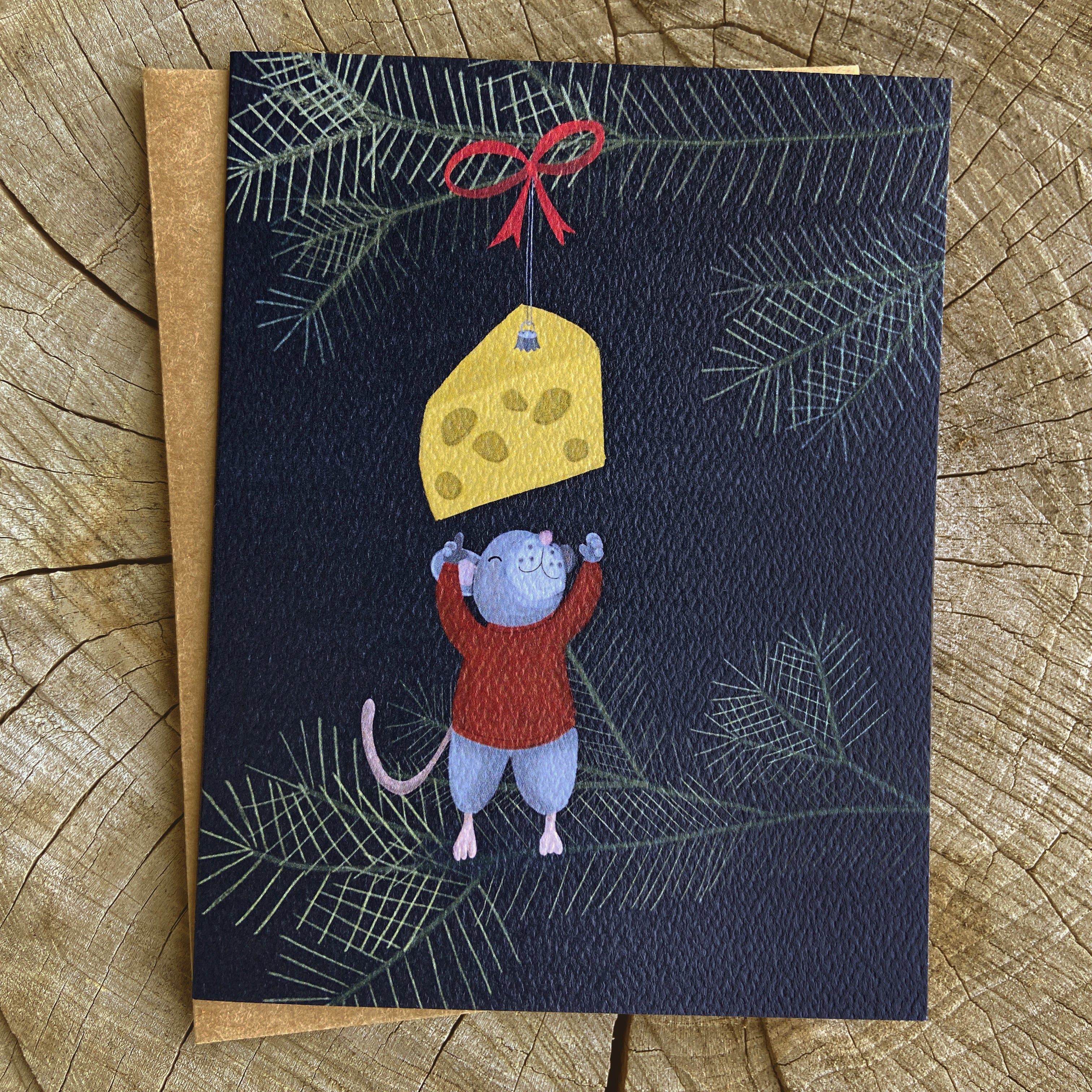 Holiday greeting card with a mouse reaching for a cheese christmas tree ornament on a dark blue background with tree branches.
