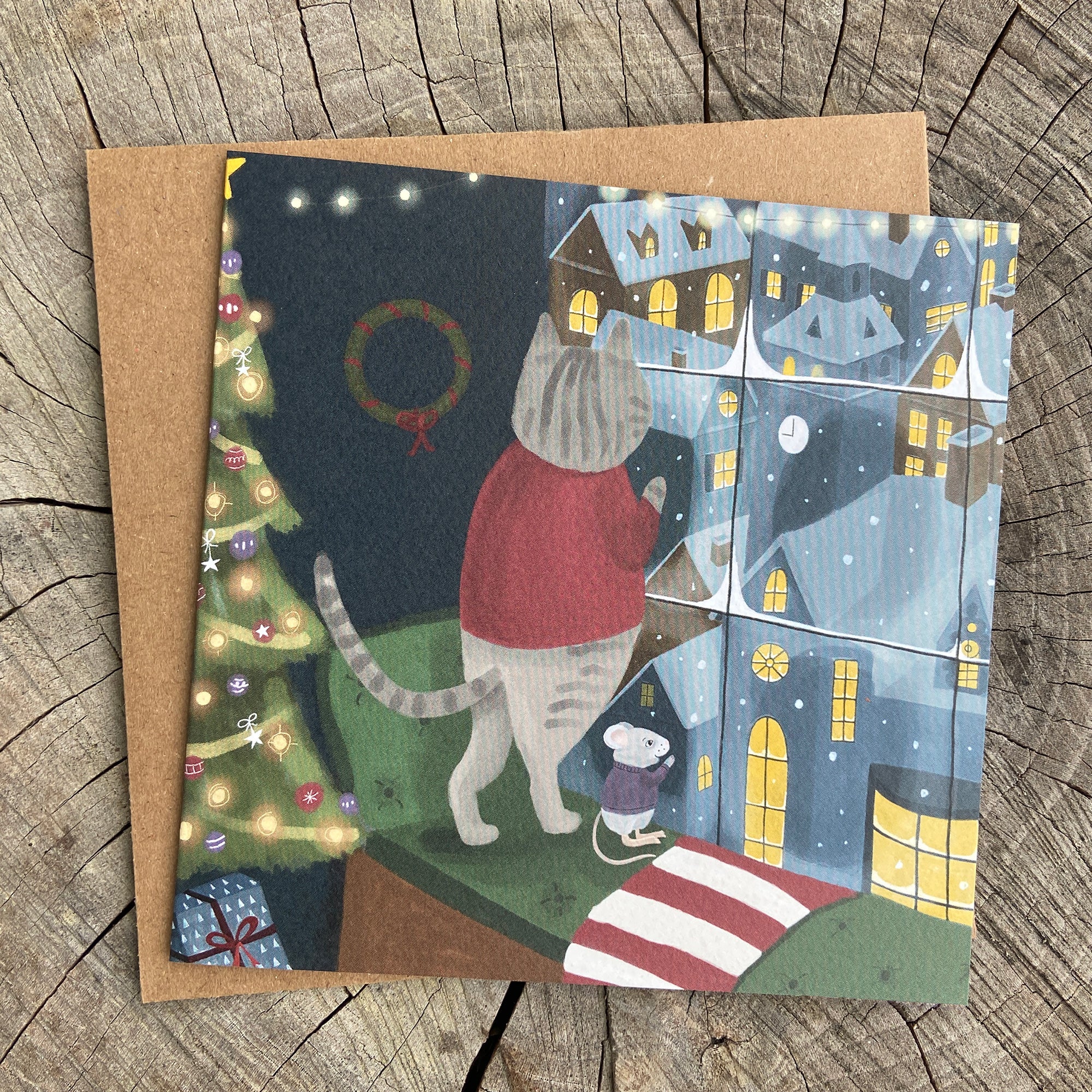 Holiday greeting card with a cat and mouse looking out a window at a snowy city scene.