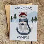 Winter greeting card featuring a cat sipping hot chocolate while wearing a scarf in a snowy setting with hand lettered type saying "Warmest Wishes"