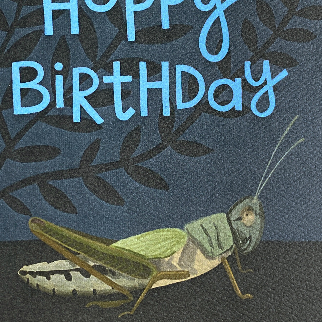 Close up of a Birthday card with a grasshopper illustration on a dark background
