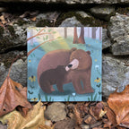 Greeting card illustration of a bear and cub in a forest scene on a stone surface with leaves.