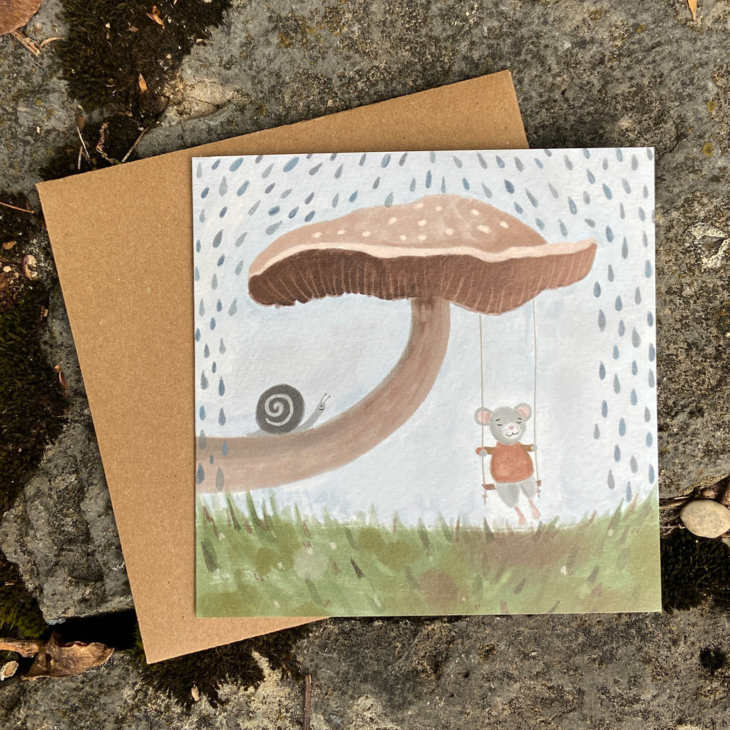 Woodland greeting card with a mushroom illustration and a mouse character, placed on a textured surface.