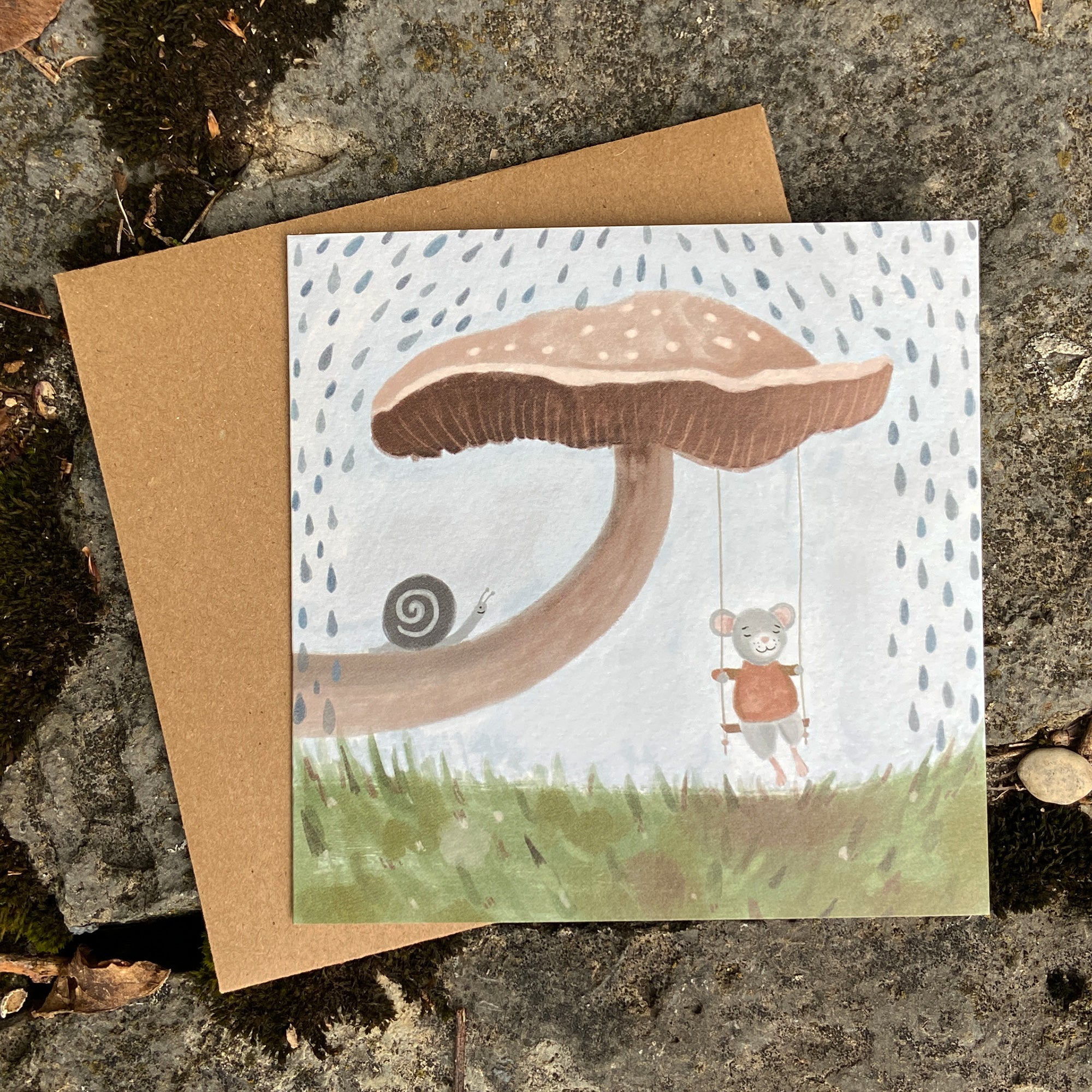 Woodland greeting card with a mushroom illustration and a mouse character, placed on a textured surface.