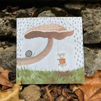 Mouse and mushroom greeting card, placed on a stone surface with leaves.