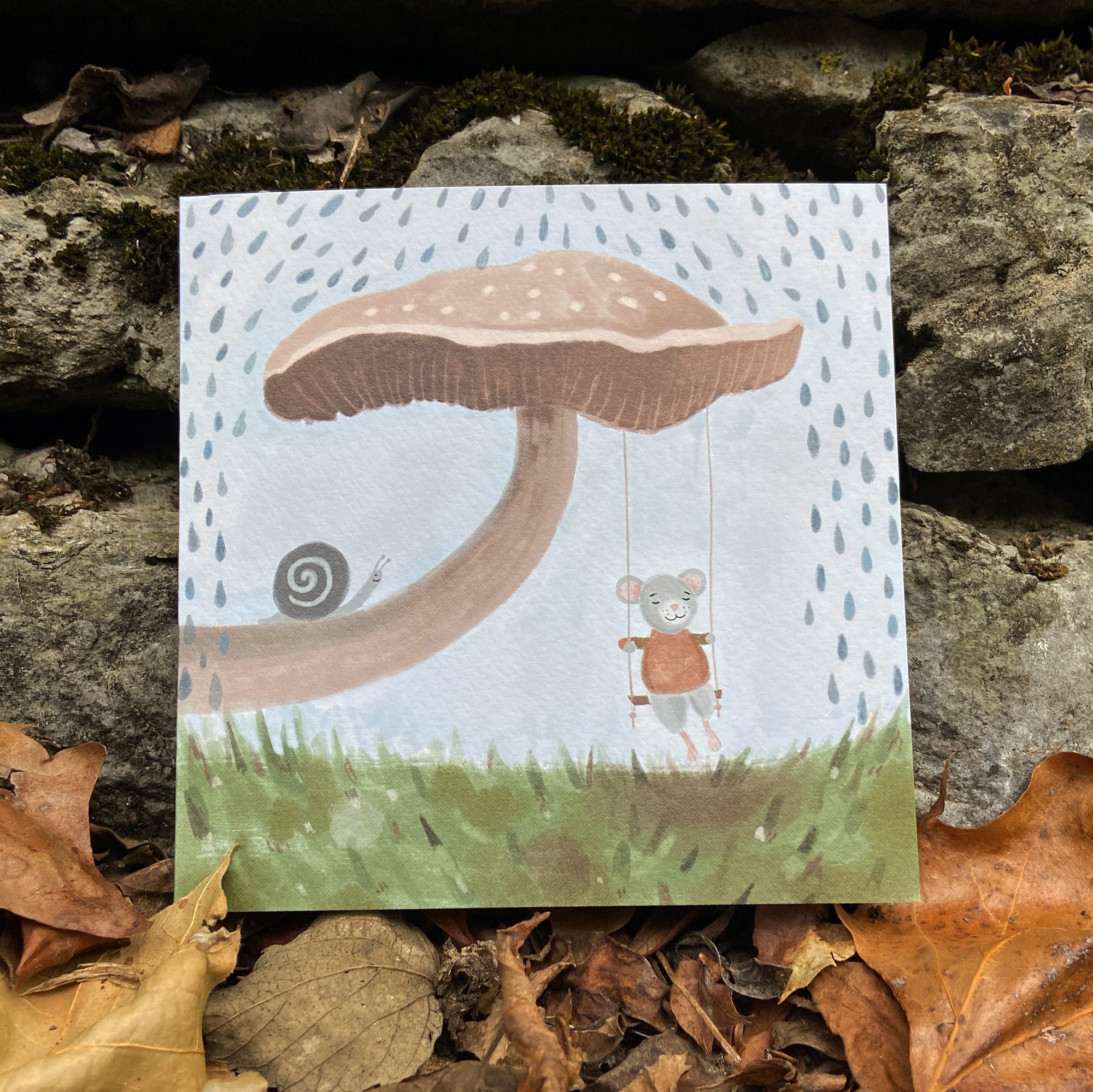 Mouse and mushroom greeting card, placed on a stone surface with leaves.