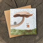 Greeting card with a mouse swinging from a mushroom with a snail nearby, on a wooden surface