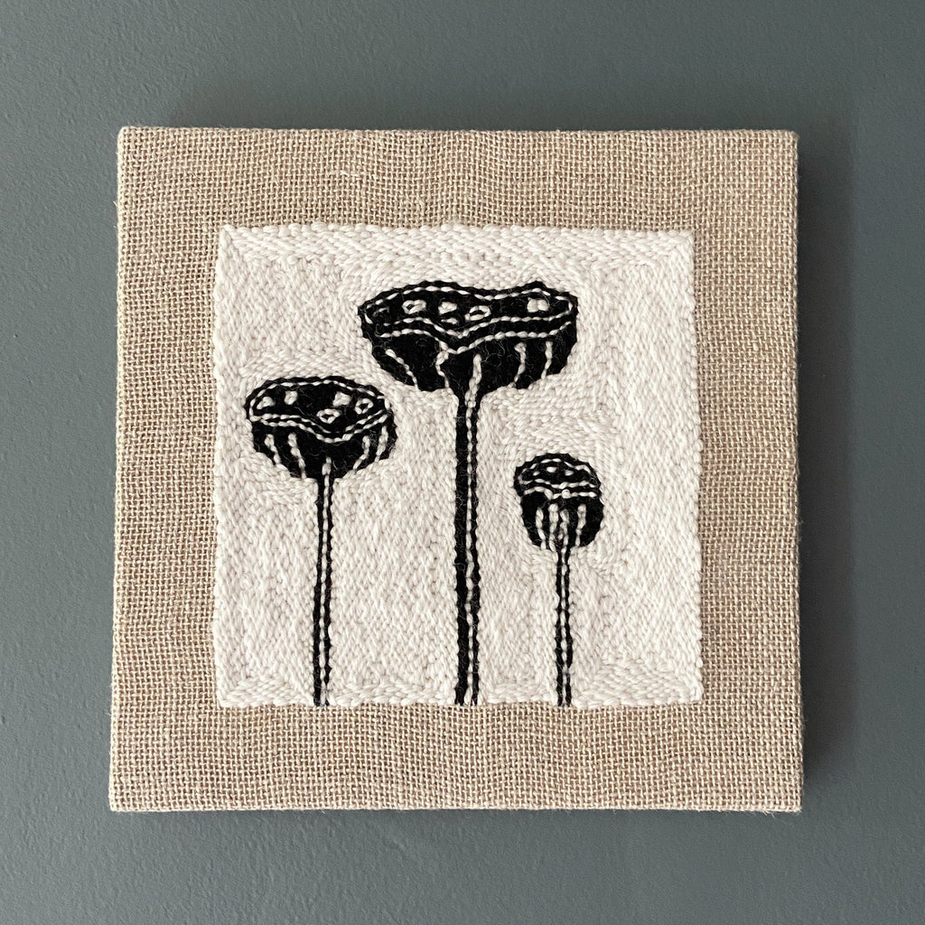 Textile art piece with black lotus pod designs on a white background and beige border.