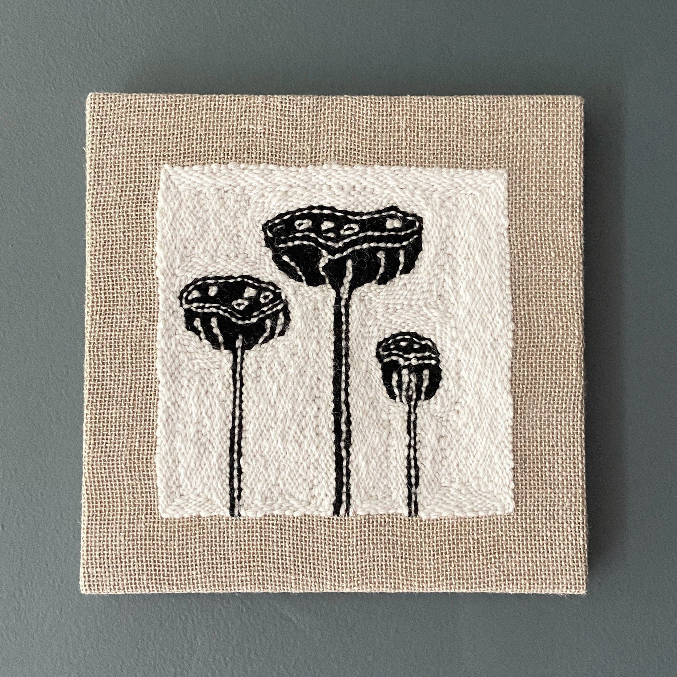 Textile art piece with black lotus pod designs on a white background and beige border.