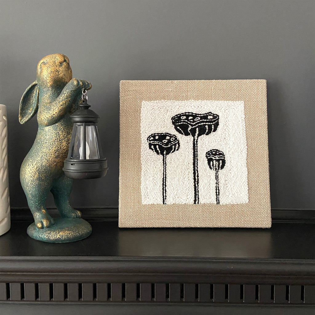 Decorative rabbit figurine with lantern and framed artwork of plants on a shelf.