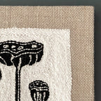 Textile art piece with black lotus pod patterns on a beige background
