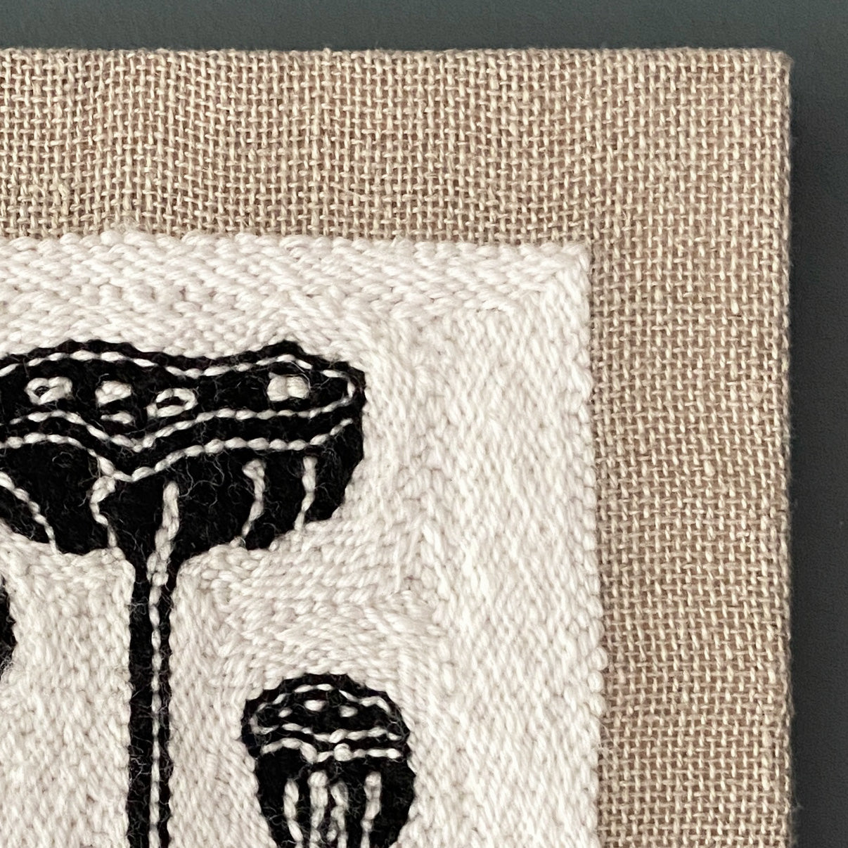 Textile art piece with black lotus pod patterns on a beige background