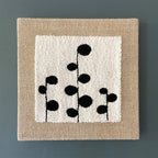 Square wall art with black floral pattern on a beige border against a blue wall
