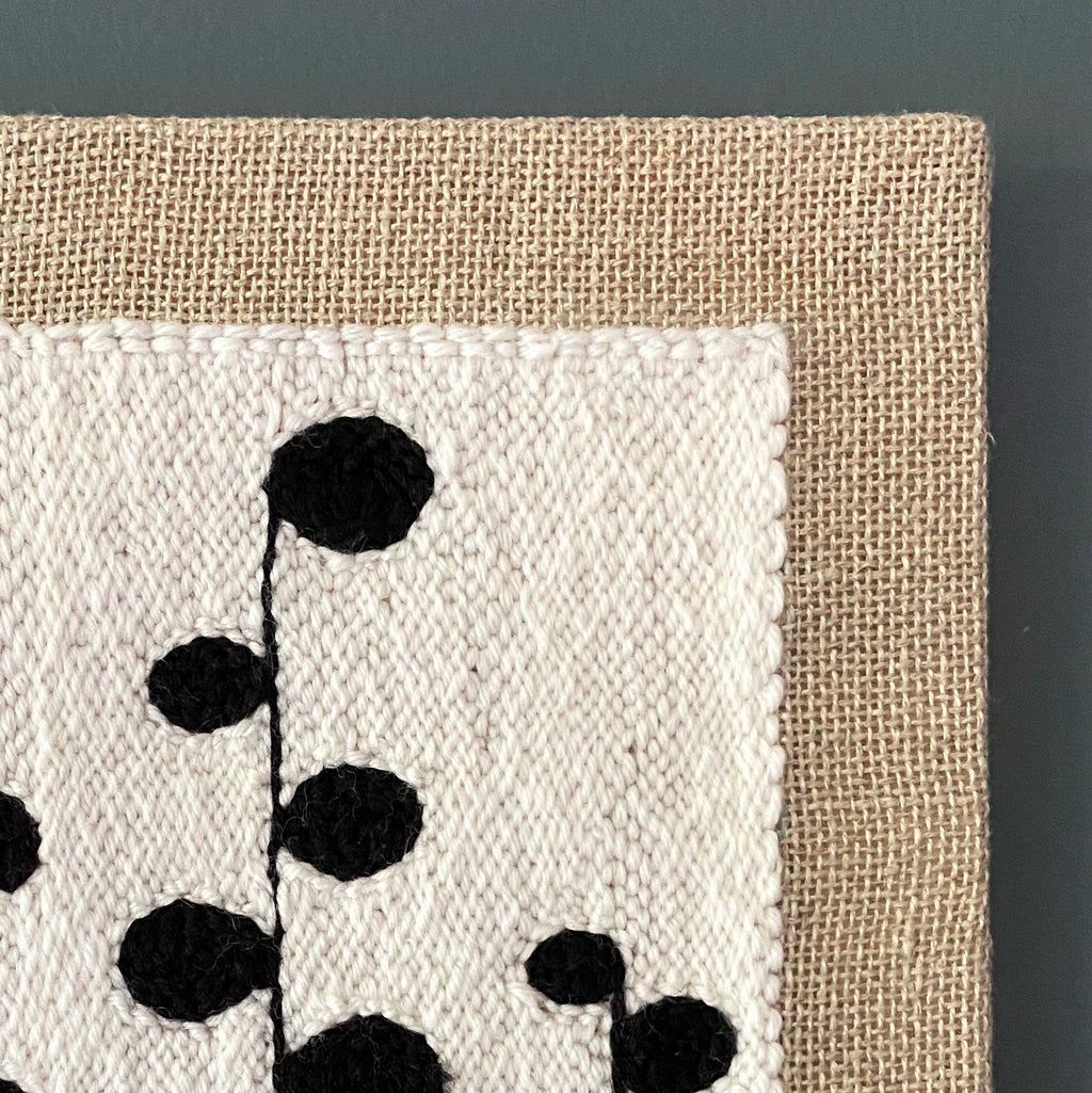 Textile art piece with black floral pattern on beige fabric against a dark background
