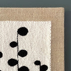 Textile art piece with black floral pattern on beige fabric against a dark background