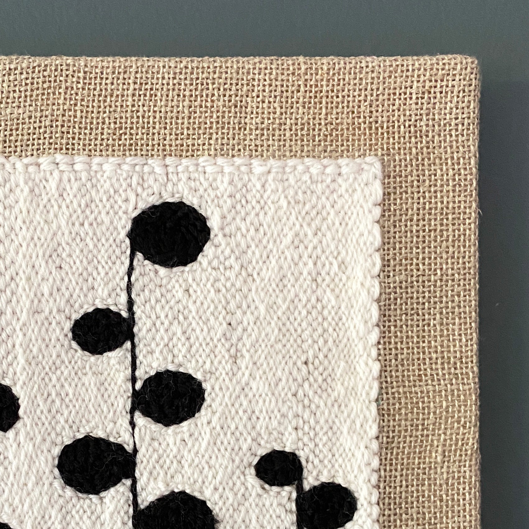 Textile art piece with black floral pattern on beige fabric against a dark background