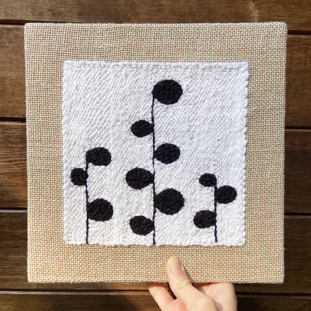 Fiber art piece with black floral pattern on a white background.