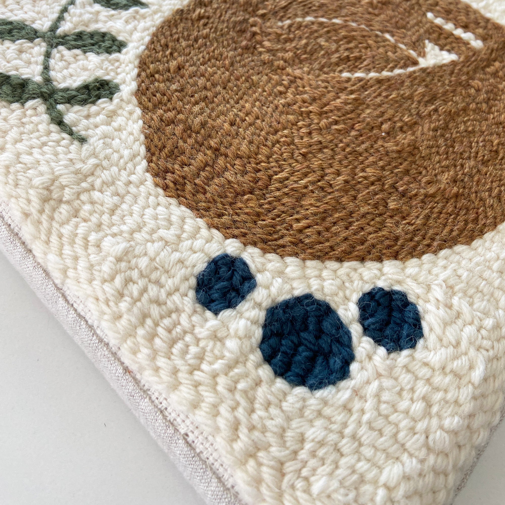 Close-up of a textured fabric art with a orange fox design and blue and green floral accents on a neutral background