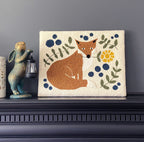 Decorative punch needle art with a fox and floral design on a dark surface against a gray wall