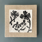 Square wall art with black floral design on a beige border against a gray background