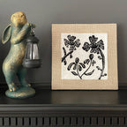 Decorative rabbit figurine with a lantern next to a framed floral artwork on a dark surface.