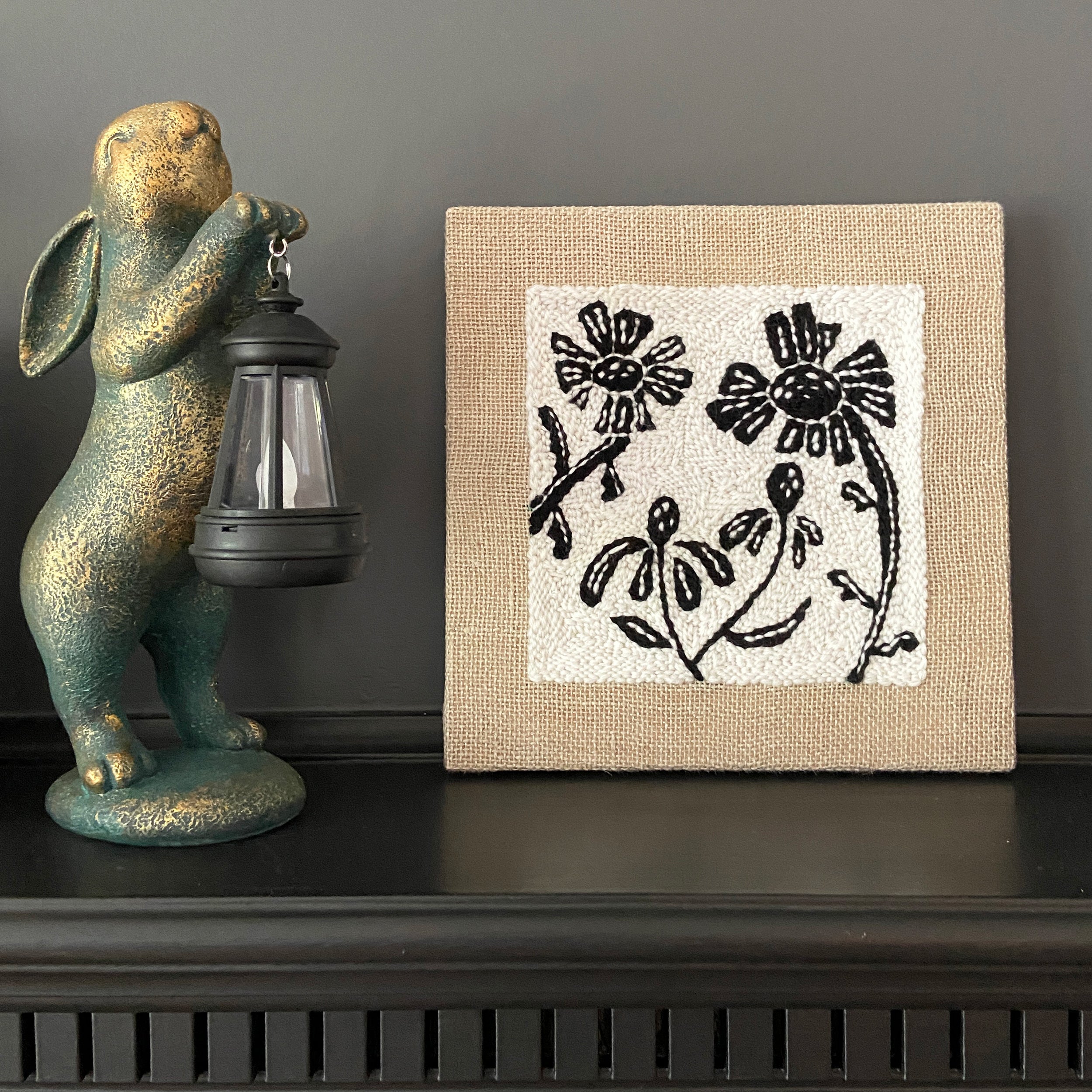 Decorative rabbit figurine with a lantern next to a framed floral artwork on a dark surface.