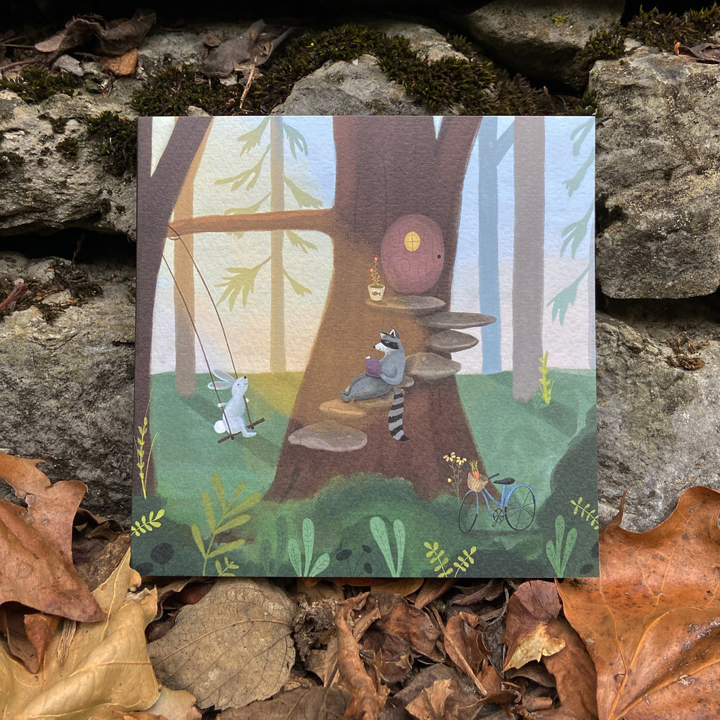 Illustrated card with woodland animals around a treehouse, on a stone surface with leaves. 