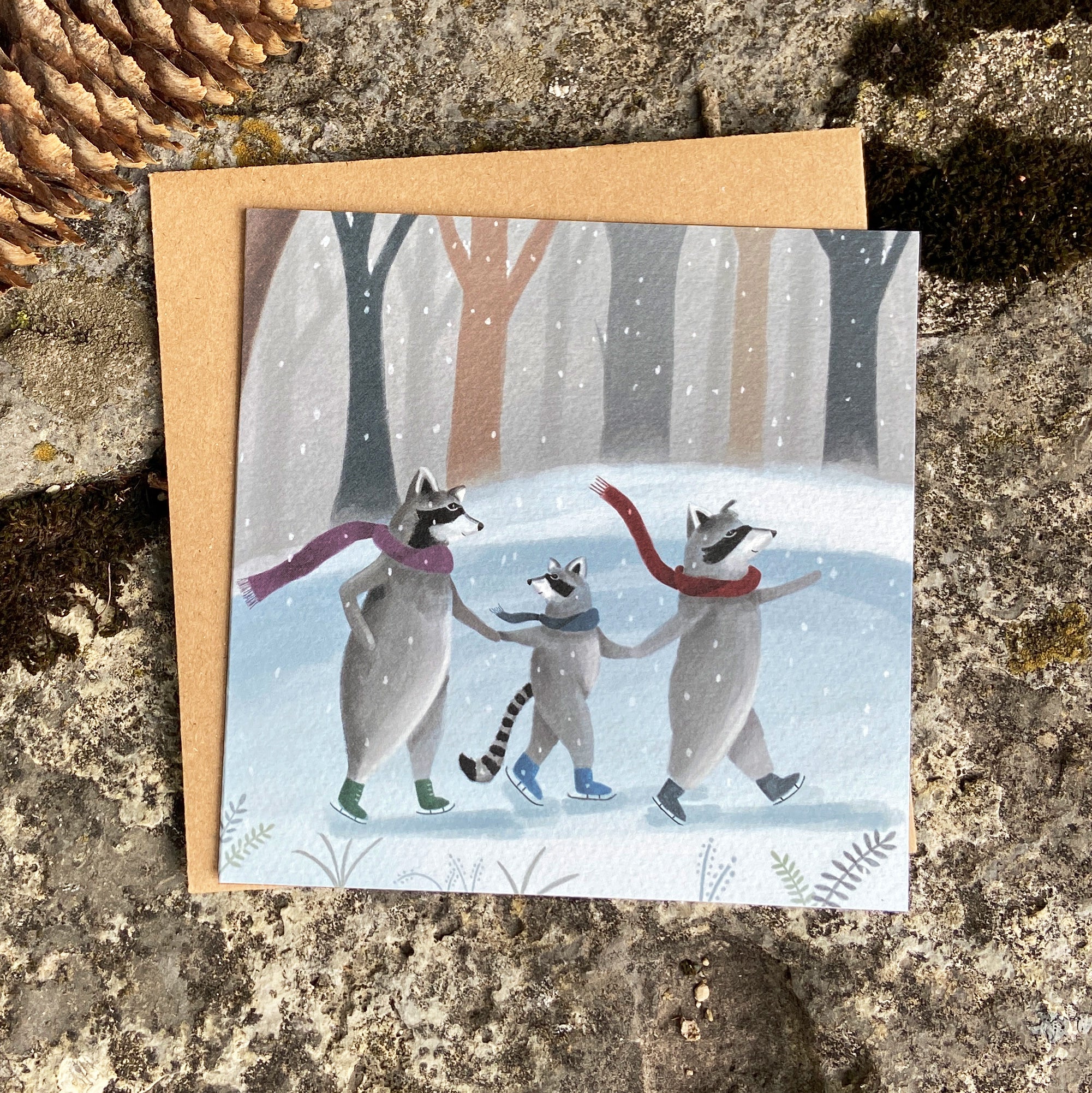 Winter greeting card with raccoons ice skating on a pond in snowy forest, on a stone background