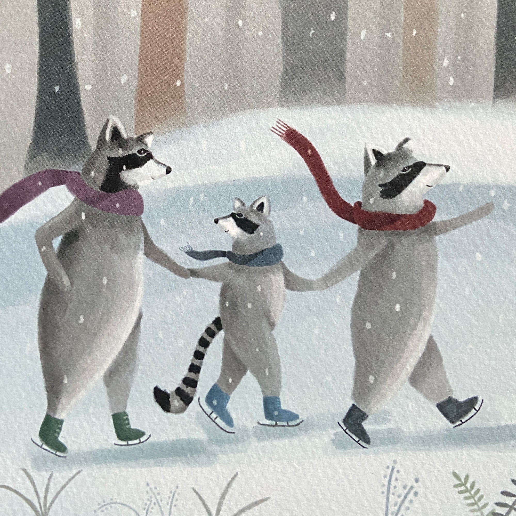 Close up of a winter greeting card featuring a raccoon family skating on ice with scarves in a snowy forest.