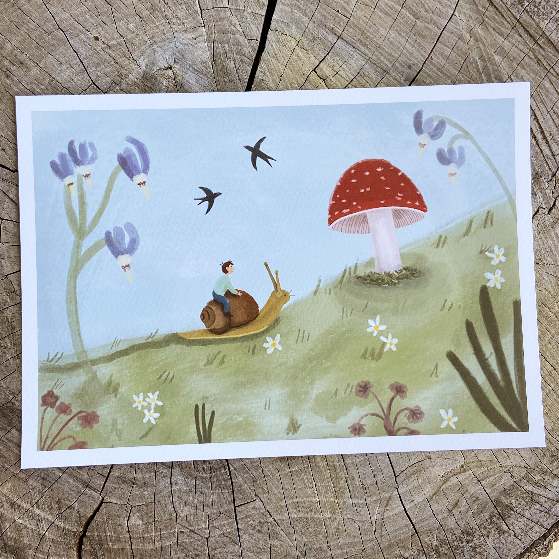 Art print with a child riding a snail, a mushroom, and flowers on a wooden surface.