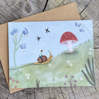 Whimsical greeting card with illustration of a child riding a snail near a mushroom, on a wooden surface