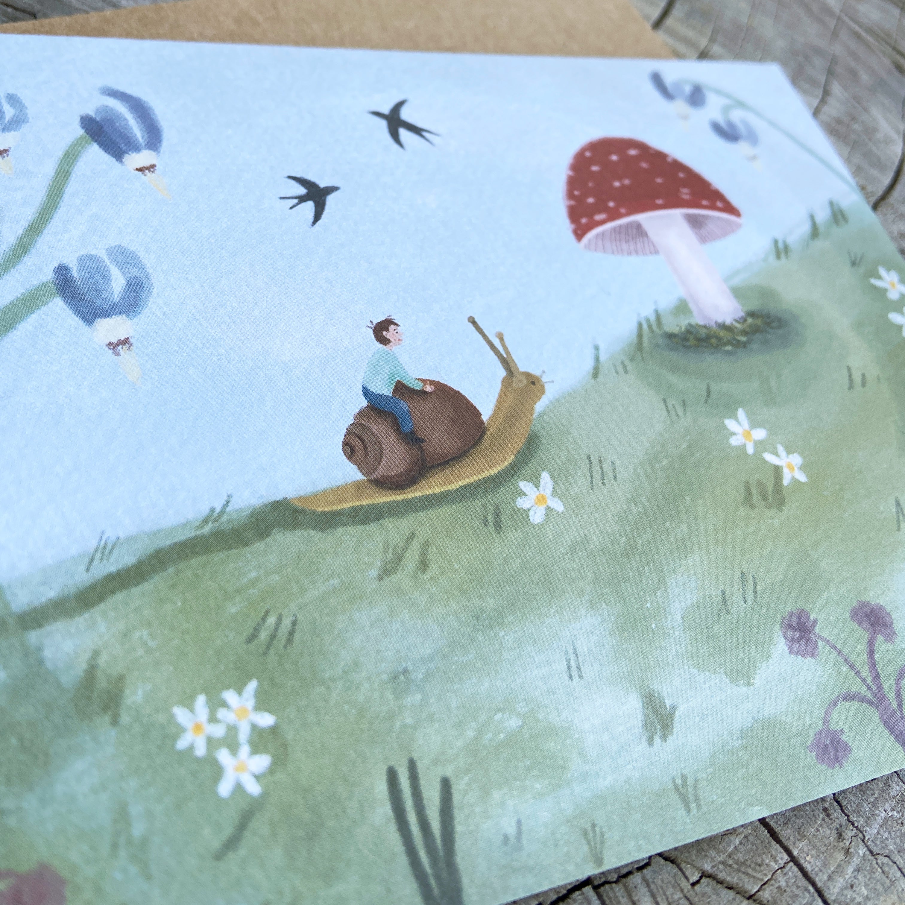 Greeting card illustration of a boy riding a snail with mushrooms and flowers in the background 