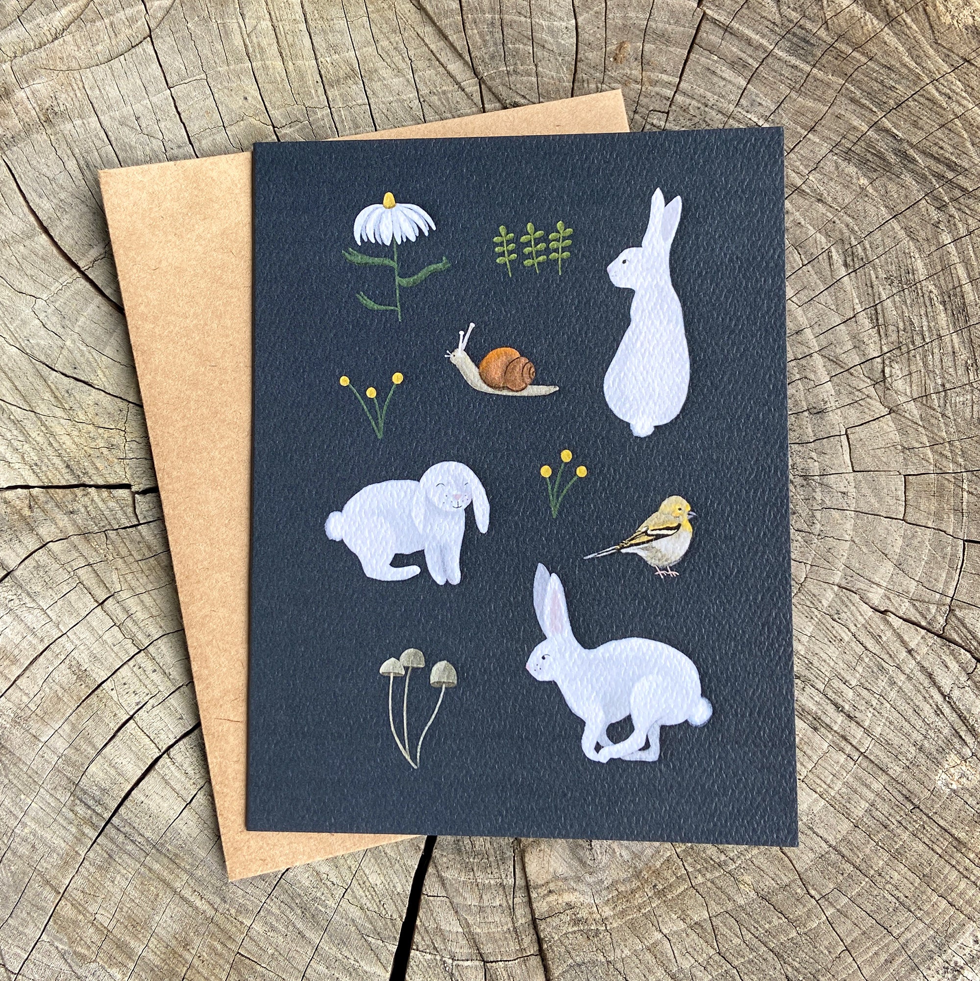 Greeting card with illustrations of rabbits, birds, snail and flowers on a wooden surface